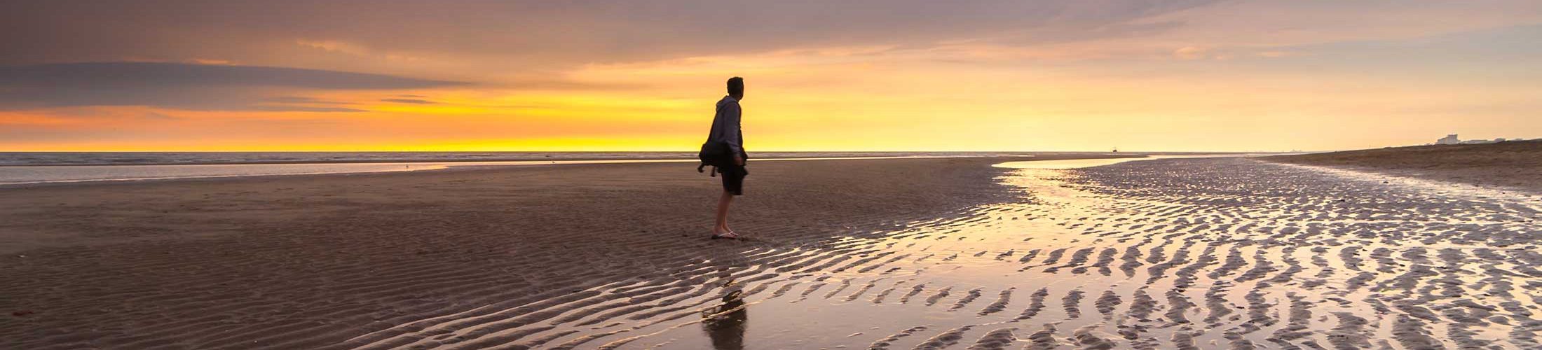 Man on beach at low tide during sunset