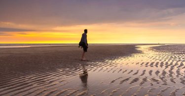 Man on beach at low tide during sunset