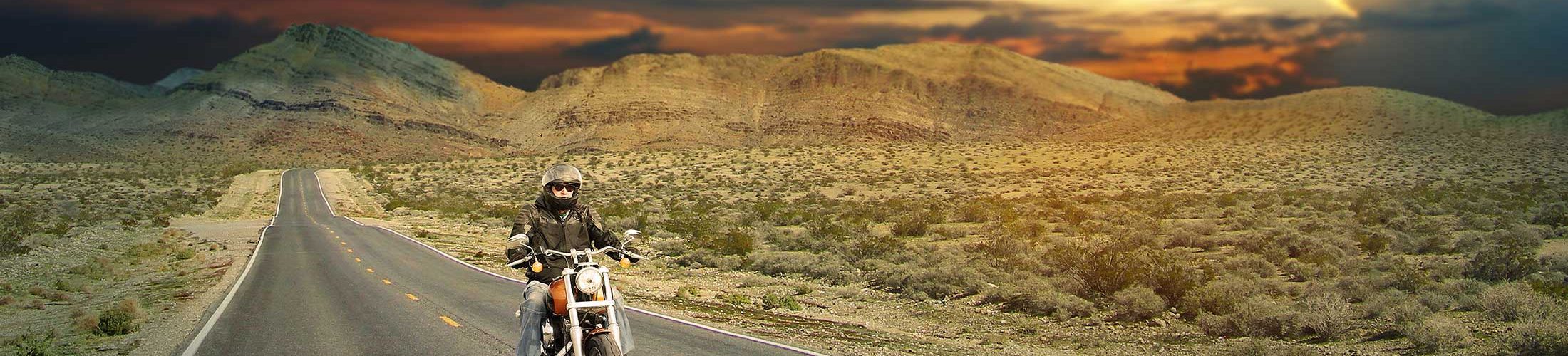 Man on motorcycle riding through the desert at sunset